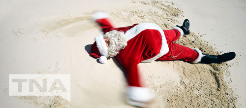 Santa making a snow angel in the sand at a beach