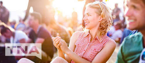 Caucasian woman clapping to music whilst sitting on the grass in the sun