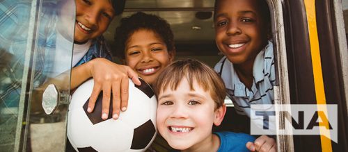 Smiling kids from school soccer team on a charter bus